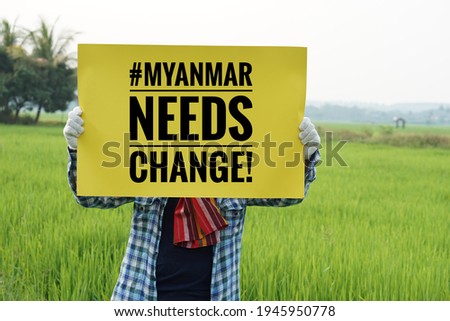 Text "#Myanmar needs change" on paper sign hold by a man at rice field. Concept protesting for democracy and against the coup in Myanmar. Royalty-Free Stock Photo #1945950778