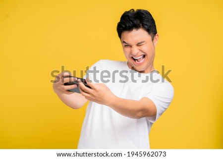 Young Asian man in casual wear is playing games with mobile phone with a yellow background isolated.