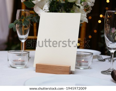 Mockup white blank space card, for greeting, table number, wedding invitation template on wedding table setting background. with clipping path Royalty-Free Stock Photo #1945972009