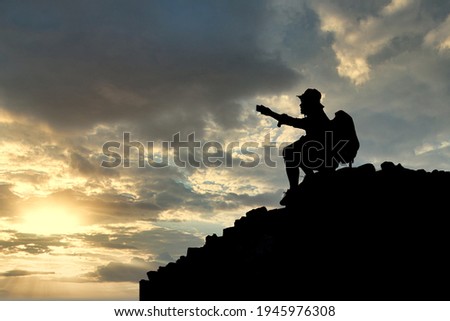 Silhouette of young male tourists Sit back and see the sunset and take pictures at the top of the mountain with your backpack. Royalty-Free Stock Photo #1945976308