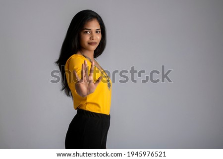 Portrait of a beautiful girl showing stop sign with palms on a grey background