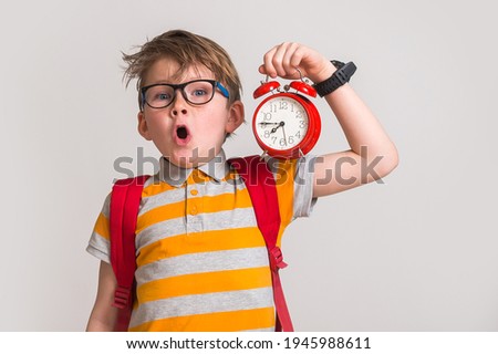 Stressed surprised and angry kid yawn and holding alarm clock. Change time. Pupil with bag and in glasses. Hurry up. Time to go to school. Royalty-Free Stock Photo #1945988611