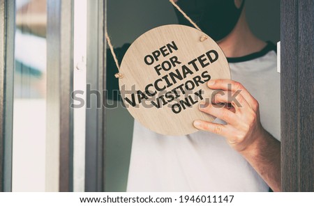 Man holds the wooden sign with text: Open for vaccinated visitors