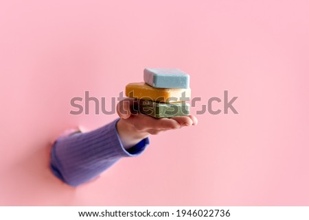 female hand hold three soaps on pink background.