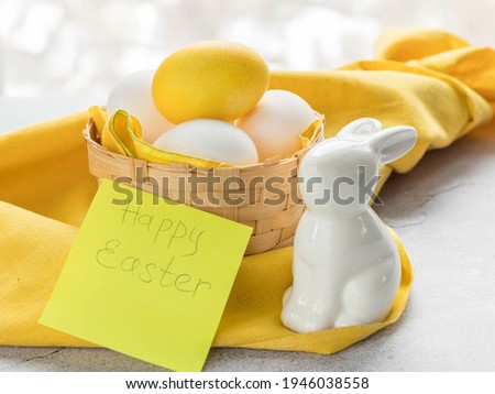 Colored Easter egg and white eggs in a basket on a yellow cloth and a white rabbit .Yellow Easter egg colored by turmeric powder .Natural dye for eggs.Easter eggs painted with natural dyes .Copy space