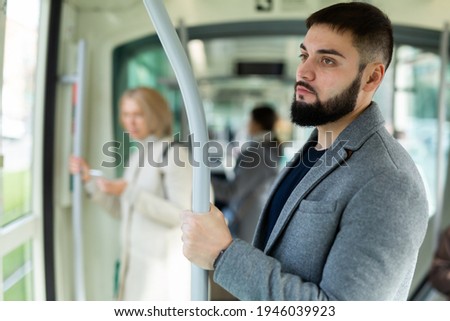 Portrait of focused guy holding on handrails in city bus during daily commute to work in autumn day