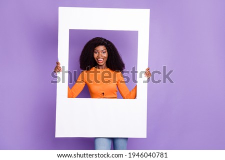 Portrait of attractive cheerful wavy-haired girl holding in hands paper frame isolated over purple violet pastel color background