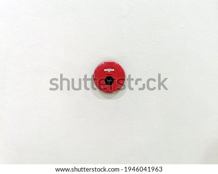 Red fire alarm bell on white cement wall.