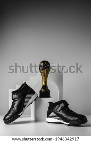 Sports shoes and a cup for the first place. Black sneakers on a gray background. Conceptual photo. Place for your text. 
Football prize. Cup on the podium. Trendy style