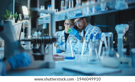 Female and Male Medical Research Scientists Have a Conversation While Conducting Experiments in Test Tubes with Liquid Samples with and in Beakers with Solid Speciments. Modern Science Laboratory. Royalty-Free Stock Photo #1946049910