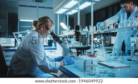 Female and Male Medical Research Scientists Have a Conversation While Conducting Experiments in Test Tubes with Liquid Samples with and in Beakers with Solid Speciments. Modern Science Laboratory. Royalty-Free Stock Photo #1946049922