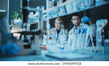 Female and Male Medical Research Scientists Have a Conversation While Conducting Experiments in Test Tubes with Liquid Samples with and in Beakers with Solid Speciments. Modern Science Laboratory. Royalty-Free Stock Photo #1946049928
