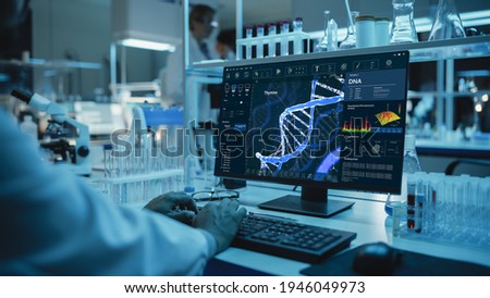 Medical Research Scientist Working on Desktop Computer with Gene Analysis Software in Modern Science Research Laboratory. Lab Engineers in White Coats Conduct Experiments in the Background.