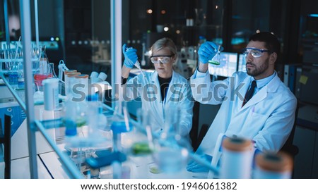 Female and Male Medical Research Scientists Have a Conversation While Conducting Experiments in Test Tubes with Liquid Samples with and in Beakers with Solid Speciments. Modern Science Laboratory. Royalty-Free Stock Photo #1946061382