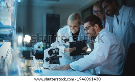Happy Male Reseach Scientist Makes an Important Discovery While Researching Samples Under the Microscope. Happy Colleagues Congratulate it and Share Success with Fellow Bioengineers. Royalty-Free Stock Photo #1946061430