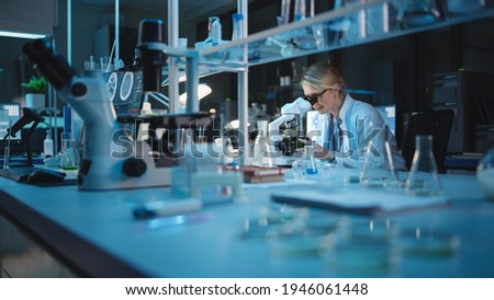 Medical Development Laboratory: Caucasian Female Scientist Looking Under Microscope, Analyzes Petri Dish Sample. Specialists Working on Medicine, Biotechnology Research in Advanced Pharma Lab Royalty-Free Stock Photo #1946061448