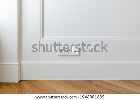Fragment of classic interior with herringbone parquet floor and panels with installed wall outlet and a network connector. Walls decorated with white moldings and skirting boards. Royalty-Free Stock Photo #1946081635