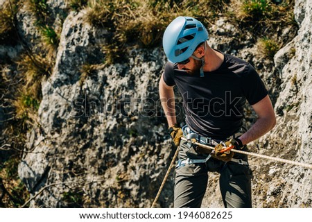Young man rappelling down a rocky cliff, he is attached on rope with a figure eight and carabiner. Extreme adventure in the mountains. Royalty-Free Stock Photo #1946082625