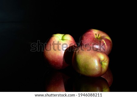 Three red apples on the dark reflecting surface, isolated on dark background. Free space for text. A low key image.