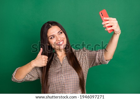 Photo of girl hold telephone take selfie raise thumb up wear plaid shirt isolated green color background