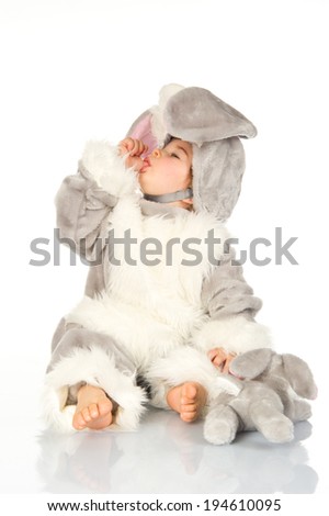 Little baby wearing bunny costume and playing with plushie on white background.