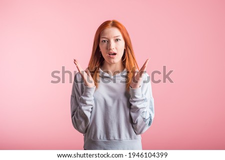 Young redhead girl shocked in studio on pink background