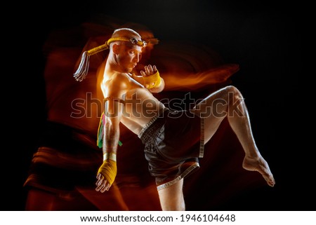 Kick. Young man thai boxer posing on dark background in neon mixed light. Fighter practicing, training in martial arts in action. Health, sport, asian culture concept. Copy space for ad. Muay thai.