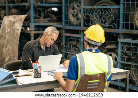 Factory manager looking at the paper with young engineer sitting front for call for blaming or consider and interview job apply or solving working problem report situation at factory work Royalty-Free Stock Photo #1946112658