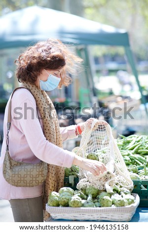 Woman with face mask buying artichokes at an outdoor market