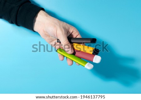 Disposable electronic cigarettes in hand closeup on a blue background with shadows. The concept of modern smoking, vaping and nicotine. Copy space Royalty-Free Stock Photo #1946137795