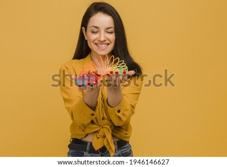 Photo of cute female with nice smile holds slinky. Wears yellow shirt, isolated yellow color background.