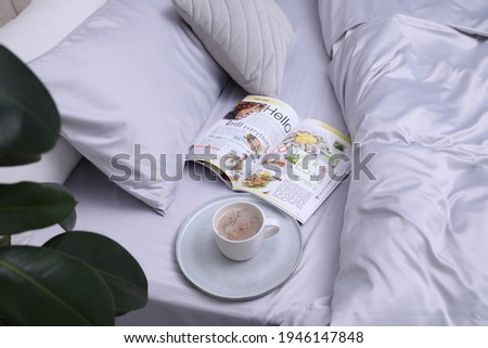 Cup of coffee and magazine on bed with soft silky bedclothes Royalty-Free Stock Photo #1946147848