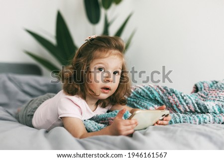 Portrait of a charming little girl who watches cartoons on her phone before going to bed. Childhood, happy time, care