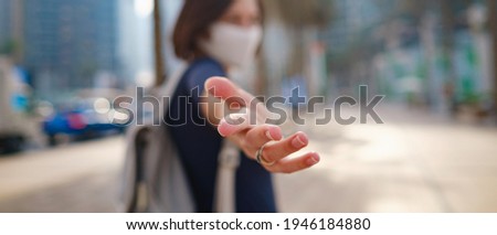Portrait of young woman wearing in blue dress and white mask for prevent virus, walk in front of skycrapers in modern city. Gesture follow me