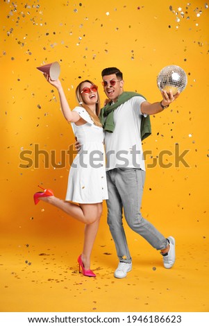 Happy couple with disco ball and confetti on yellow background