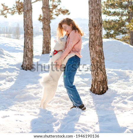 A curly-haired girl walks with a white akita in a snowy forest.
