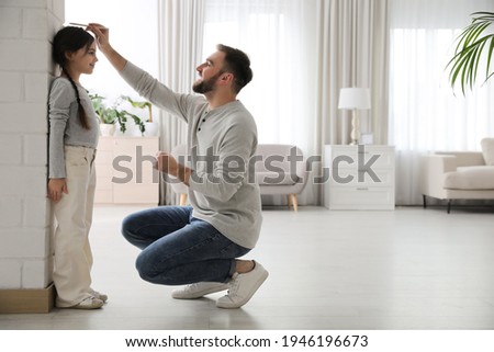 Father measuring daughter's height near white brick pillar at home, space for text Royalty-Free Stock Photo #1946196673