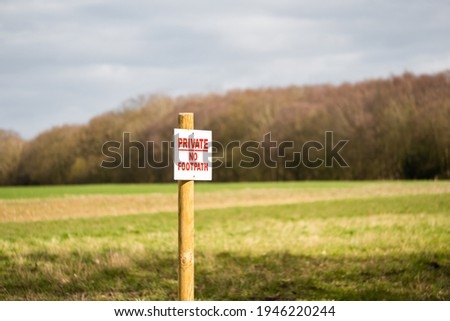 Shallow focus of a Private No Footpath sign seen at the edge of new crops planted on a farm field.