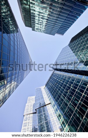 Modern office buildings against bright blue sky. Bottom-up view. Glass facades of skyscrapers with contrasting highlights and reflections. Economy development, finance and business concept. Downtown. Royalty-Free Stock Photo #1946226238