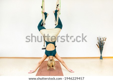 a woman hangs upside down in a hammock with her back to the camera against a light-colored wall in the room Royalty-Free Stock Photo #1946229457