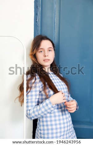 Portrait of   beautiful young girl in   blue checkered dress against   blue  door background
