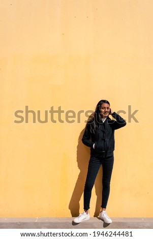 Portrait of a beautiful Young Latin woman with black hair and casual clothes leaning against a yellow background with space for writing.