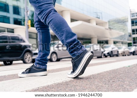 Close-up of the feet of a man in black sneakers crossing a street on the zebra or pedestrian path. Royalty-Free Stock Photo #1946244700