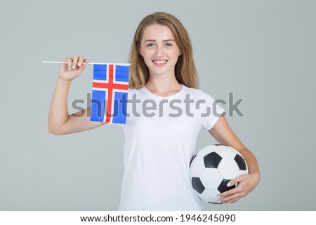 Young woman with the flag of Iceland and a soccer ball in her hands, looking directly into the camera, isolated on gray background. Icelandic women's football.