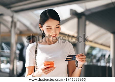Business people shopping via online application media concept. Happy smile young adult asian woman consumer using creadit card and smartphone. City on day background with copy space.