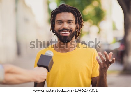 Photo portrait of young man smiling giving interview to journalist talking in microphone on street Royalty-Free Stock Photo #1946277331