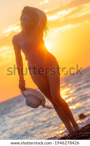 Silhouette of a girl in a swimsuit with a hat near the sea at sunset.