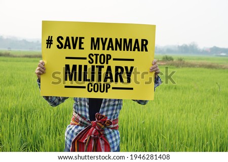 Text "#Save Myanmar stop military coup" on paper sign hold by a man at green paddy field. Concept protesting for democracy and against the coup in Myanmar. Royalty-Free Stock Photo #1946281408