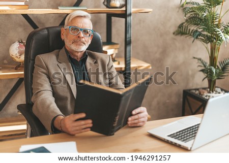 Read at your leisure. Grandpa is holding a book, a popular bestseller. Aged literary critic. Royalty-Free Stock Photo #1946291257