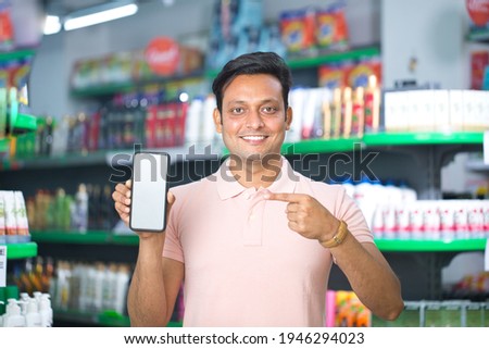Man pointing at blank mobile phone screen in supermarket Royalty-Free Stock Photo #1946294023
